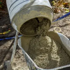 Beton wylewany z betoniarki do taczki. Właściwe proporcje cementu i piasku kluczowe dla wytrzymałości.