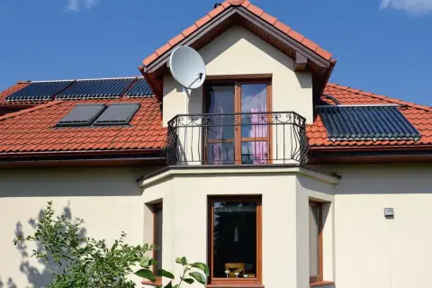 Dom z balkonem i oknami, na dachu kolektory słoneczne. Czy to wykusz co to? Tak, to element architektoniczny.