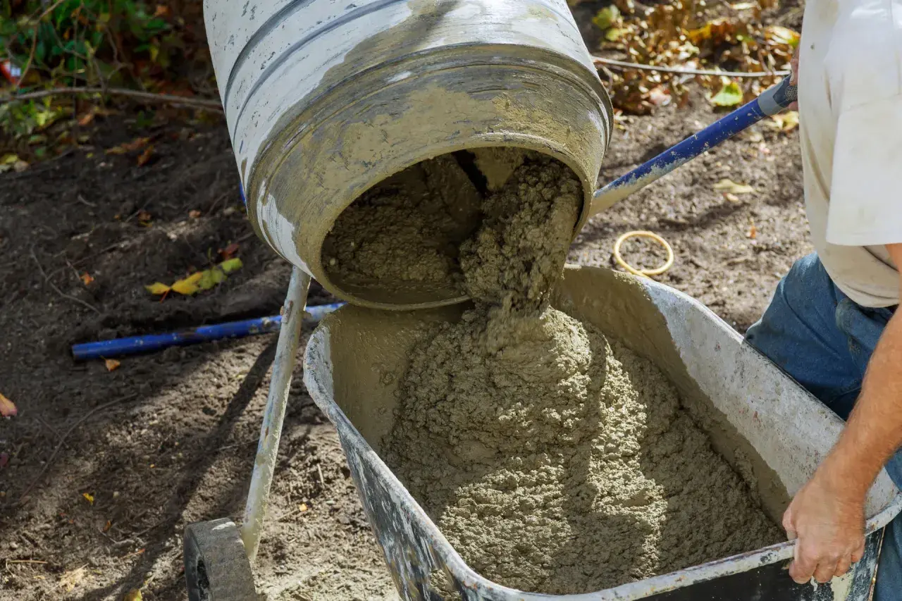 Beton wylewany z betoniarki do taczki. Właściwe proporcje cementu i piasku kluczowe dla wytrzymałości.