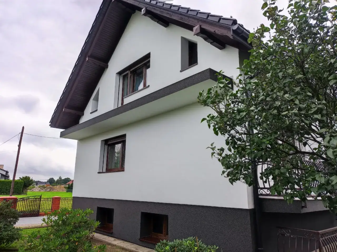 Nowy tynk i ciemny cokół to kluczowe elementy, które obejmuje termomodernizacja budynku, poprawiając jego wygląd i izolację.