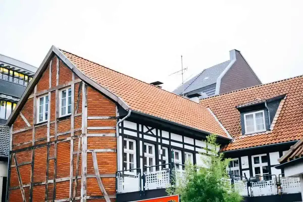 Urokliwy dom szachulcowy z ceglanymi ścianami i białymi belkami, otoczony innymi budynkami.